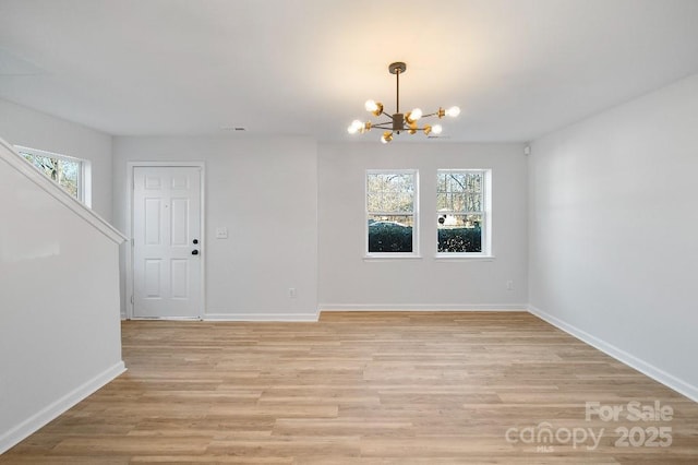 unfurnished room with a healthy amount of sunlight, an inviting chandelier, and light hardwood / wood-style floors