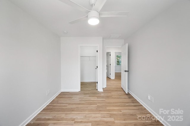 unfurnished bedroom with light hardwood / wood-style flooring, a closet, ceiling fan, and a walk in closet