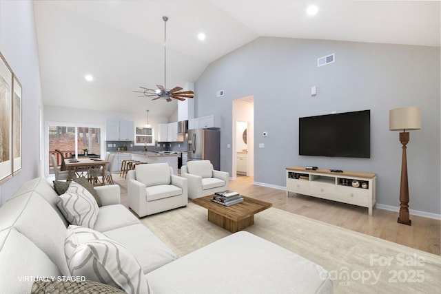 living room with light wood-type flooring, ceiling fan, high vaulted ceiling, and sink