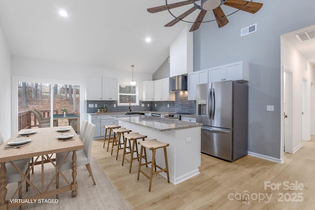 kitchen with white cabinets, a kitchen island, wall chimney range hood, stainless steel appliances, and high vaulted ceiling