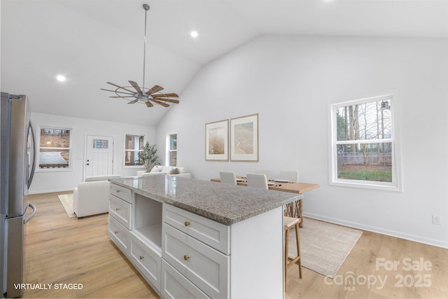 kitchen with a kitchen bar, light wood-type flooring, pendant lighting, light stone counters, and stainless steel fridge