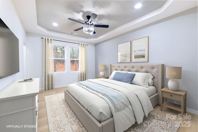 bedroom featuring ceiling fan, a tray ceiling, and light wood-type flooring