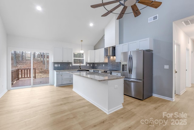 kitchen featuring appliances with stainless steel finishes, white cabinets, high vaulted ceiling, wall chimney range hood, and a kitchen island