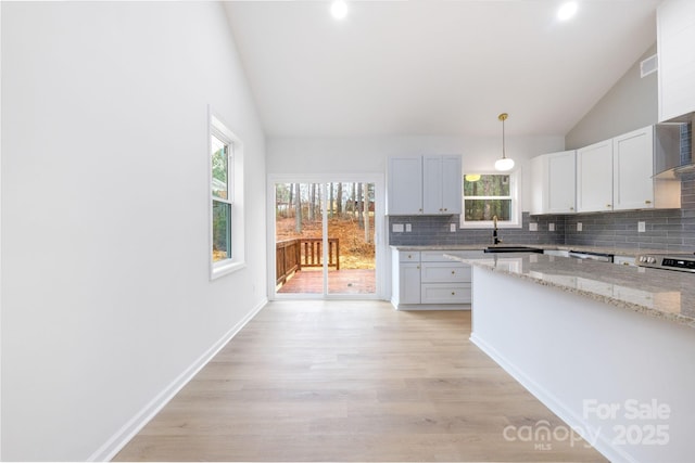 kitchen featuring vaulted ceiling, white cabinetry, light stone counters, and decorative light fixtures