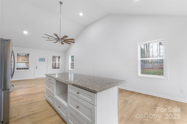 kitchen with light stone countertops, pendant lighting, light wood-type flooring, stainless steel refrigerator, and vaulted ceiling