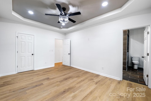 unfurnished bedroom with ceiling fan, light wood-type flooring, ensuite bathroom, and a raised ceiling