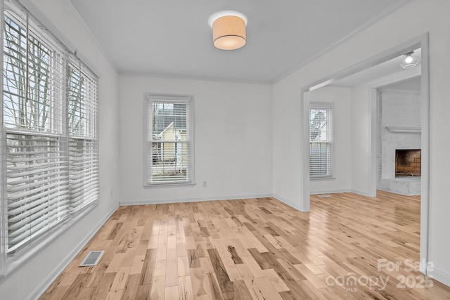 unfurnished room featuring a brick fireplace, ornamental molding, and light wood-type flooring