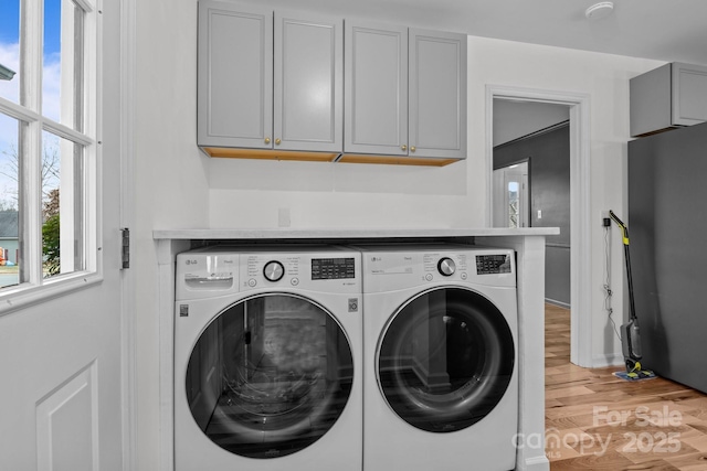 clothes washing area with washer and dryer, cabinets, and hardwood / wood-style floors