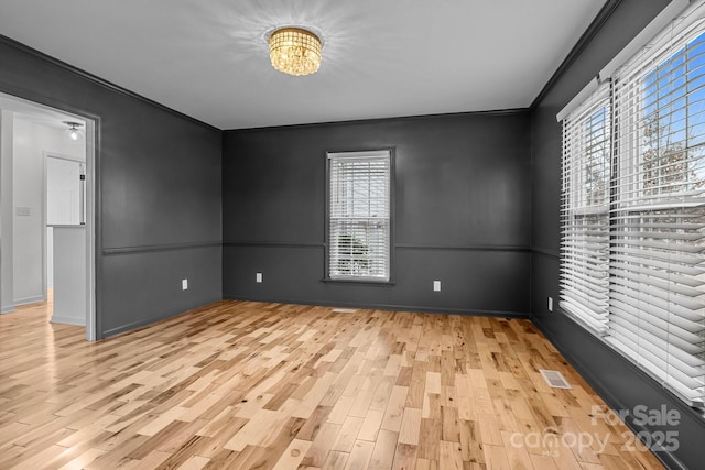 empty room with crown molding, light wood-type flooring, and a wealth of natural light