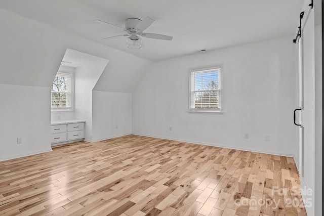 additional living space with ceiling fan, a barn door, light hardwood / wood-style floors, and lofted ceiling