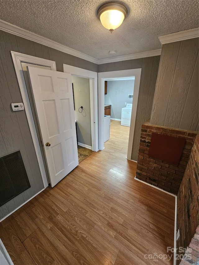 hallway featuring light hardwood / wood-style flooring, crown molding, a textured ceiling, and independent washer and dryer