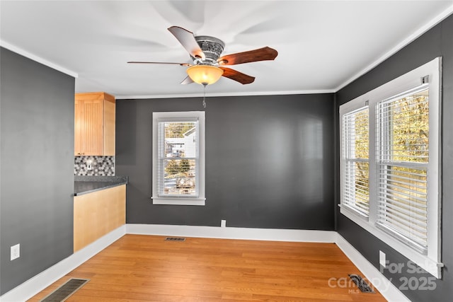 unfurnished room with ceiling fan, a wealth of natural light, crown molding, and light wood-type flooring