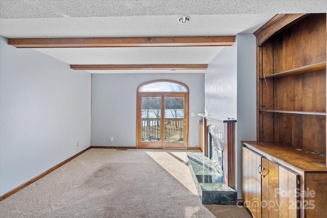 unfurnished living room featuring beamed ceiling, carpet floors, and a textured ceiling