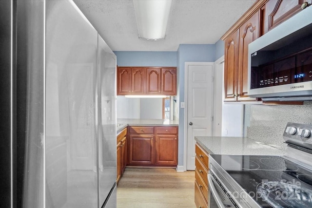 kitchen with appliances with stainless steel finishes, light hardwood / wood-style floors, and a textured ceiling