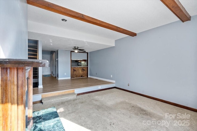 unfurnished living room featuring ceiling fan, beamed ceiling, and carpet flooring
