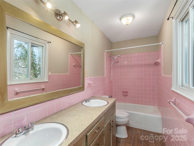 full bathroom featuring vanity, tiled shower / bath combo, tile walls, and toilet