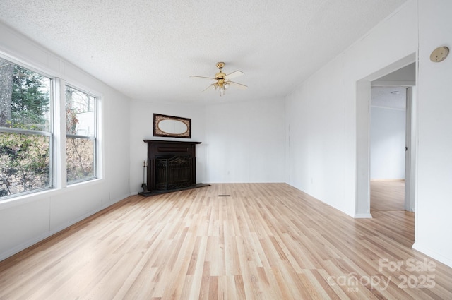 unfurnished living room with ceiling fan, light hardwood / wood-style floors, and a textured ceiling