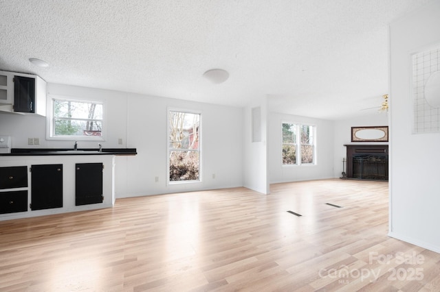 unfurnished living room with sink, a textured ceiling, and light hardwood / wood-style flooring