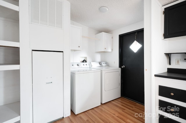 washroom with cabinets, separate washer and dryer, light wood-type flooring, and a textured ceiling