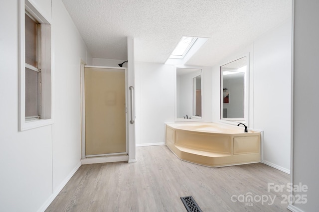 bathroom with hardwood / wood-style flooring, a skylight, plus walk in shower, and a textured ceiling