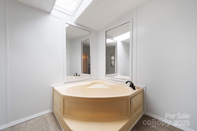 bathroom featuring a skylight, a bathing tub, hardwood / wood-style floors, and a textured ceiling