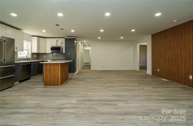 kitchen with light hardwood / wood-style floors, appliances with stainless steel finishes, white cabinetry, decorative light fixtures, and a kitchen island