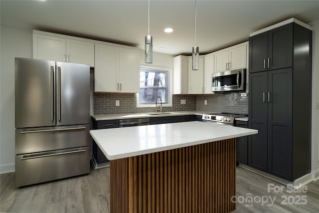 kitchen featuring appliances with stainless steel finishes, white cabinets, a kitchen island, sink, and pendant lighting