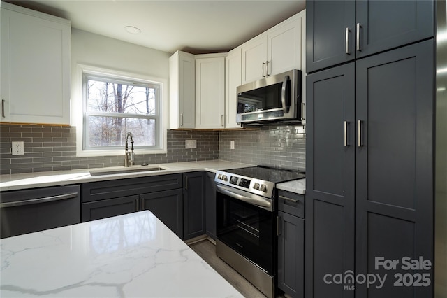 kitchen with light stone countertops, white cabinetry, stainless steel appliances, tasteful backsplash, and sink