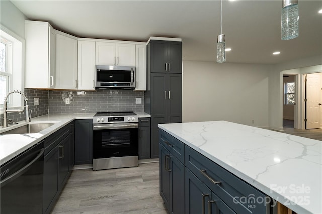 kitchen with appliances with stainless steel finishes, decorative light fixtures, sink, white cabinets, and tasteful backsplash