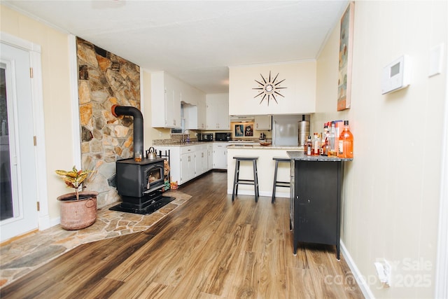 kitchen with white cabinets, dark wood-type flooring, a wood stove, light countertops, and a kitchen bar