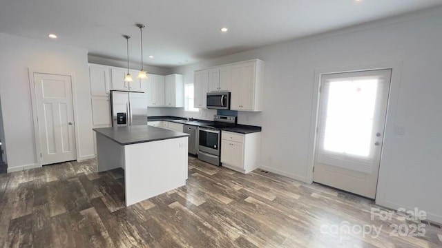 kitchen featuring dark countertops, dark wood-style floors, a center island, stainless steel appliances, and white cabinetry