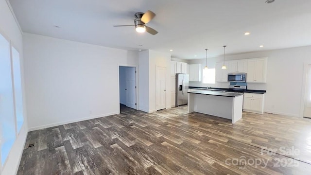 kitchen with a center island, stainless steel appliances, dark countertops, open floor plan, and wood finished floors