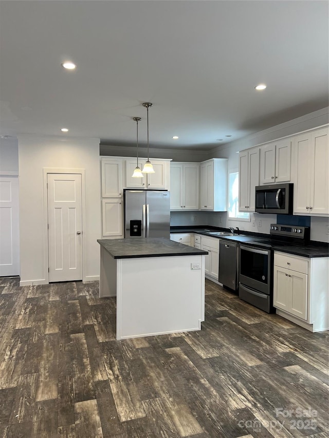 kitchen with dark wood-style flooring, decorative light fixtures, dark countertops, appliances with stainless steel finishes, and white cabinets