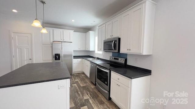 kitchen with dark countertops, appliances with stainless steel finishes, dark wood-type flooring, white cabinets, and a sink