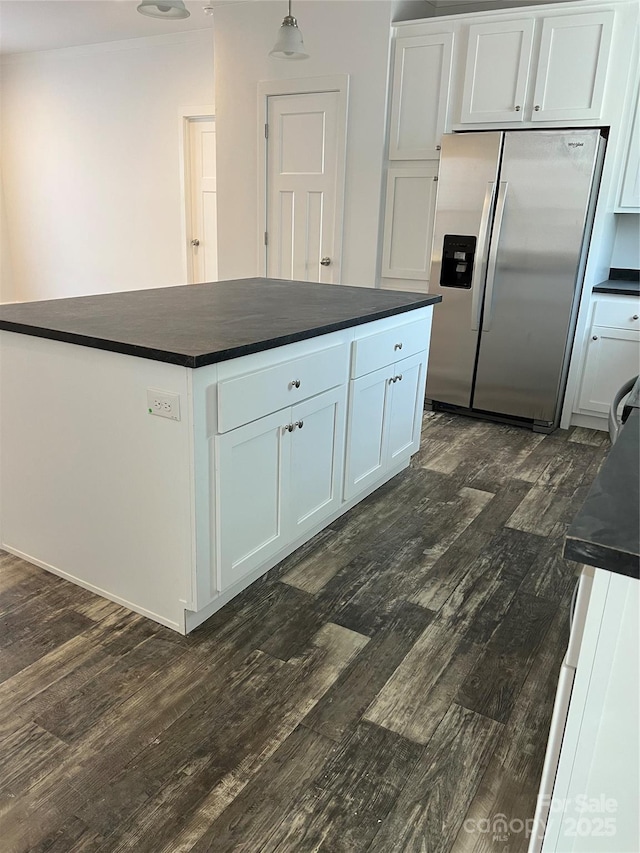 kitchen featuring stainless steel fridge, white cabinets, dark countertops, dark wood-style floors, and hanging light fixtures