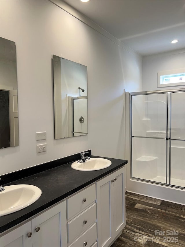 full bath with double vanity, a sink, a shower stall, and wood finished floors