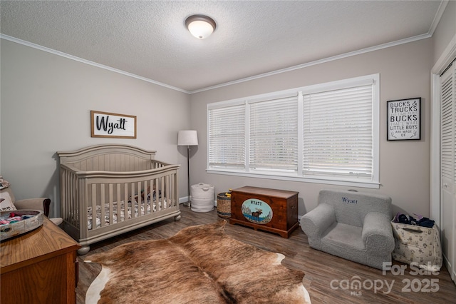 bedroom featuring a crib, dark wood-type flooring, a textured ceiling, ornamental molding, and a closet