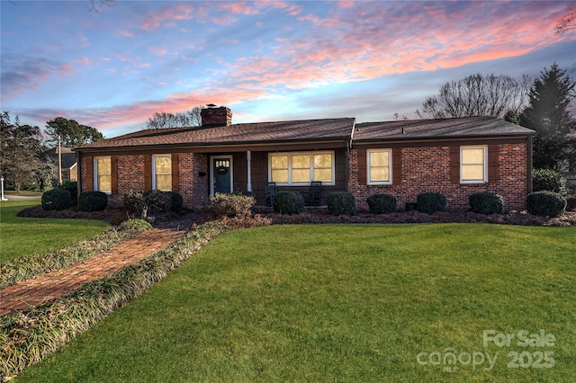 ranch-style house featuring a chimney, brick siding, and a lawn