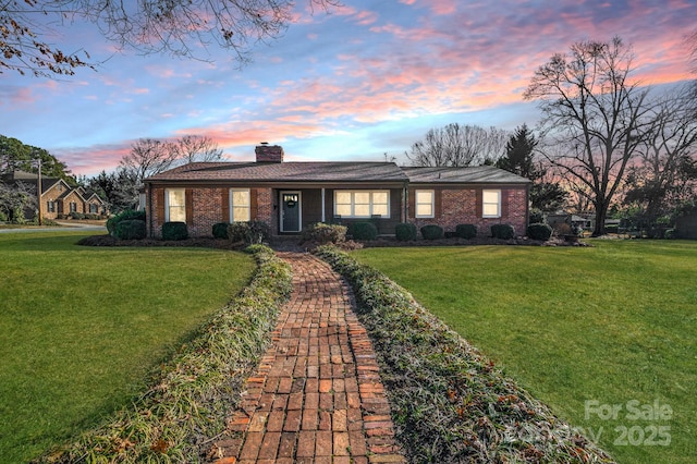 ranch-style house featuring a chimney, brick siding, and a front yard