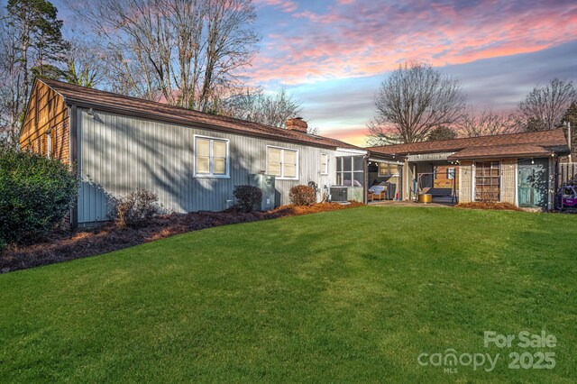 back of house at dusk featuring a chimney, central AC unit, and a yard