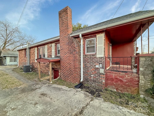 view of home's exterior featuring central AC, brick siding, and a chimney