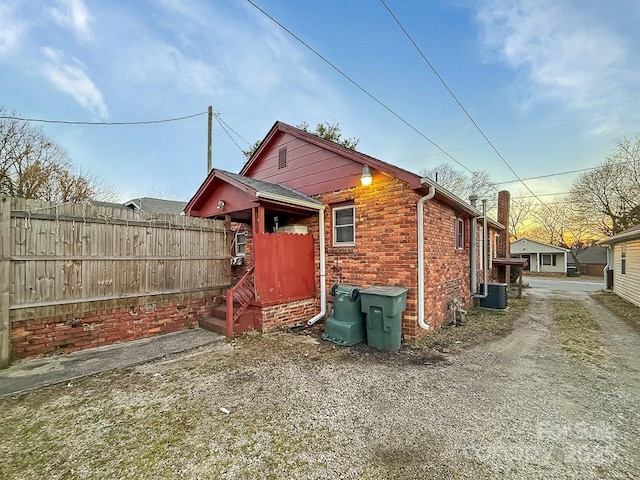 view of property exterior with cooling unit, brick siding, and fence