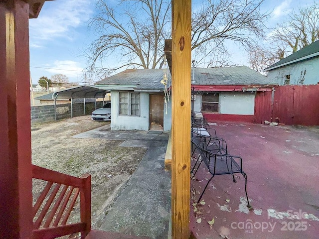 exterior space featuring a carport, roof with shingles, and fence