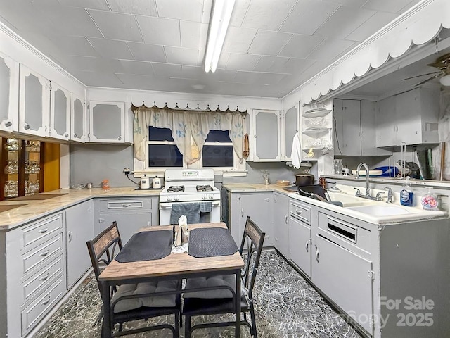 kitchen with a sink, white cabinetry, light countertops, ornamental molding, and white gas range oven