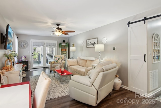 living room featuring dark wood-type flooring, a barn door, and ceiling fan