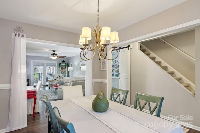 dining room with ceiling fan with notable chandelier, dark wood-type flooring, and a barn door