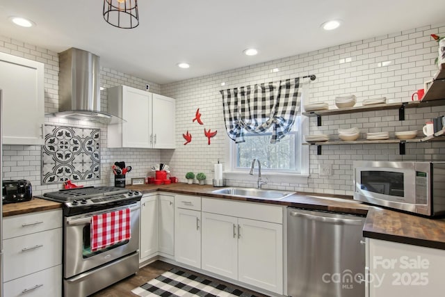 kitchen featuring appliances with stainless steel finishes, white cabinetry, sink, wooden counters, and wall chimney range hood