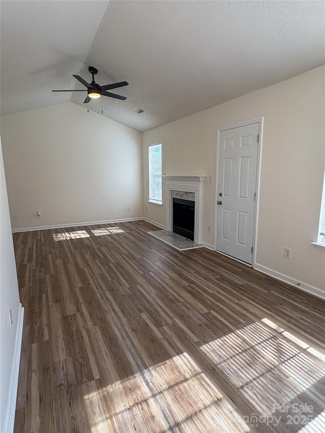 unfurnished living room with vaulted ceiling, dark hardwood / wood-style flooring, ceiling fan, a premium fireplace, and a textured ceiling