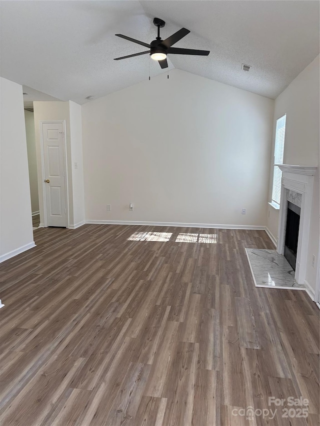 unfurnished living room featuring dark wood-type flooring, vaulted ceiling, a textured ceiling, ceiling fan, and a high end fireplace