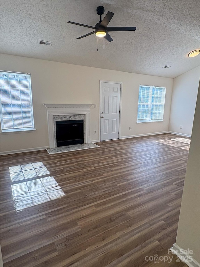 unfurnished living room with a premium fireplace, plenty of natural light, dark hardwood / wood-style floors, and ceiling fan